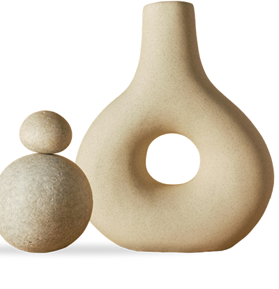 A textured beige ceramic vase with a rounded body and a central hole stands beside two stacked stone-like spheres on a plain background.