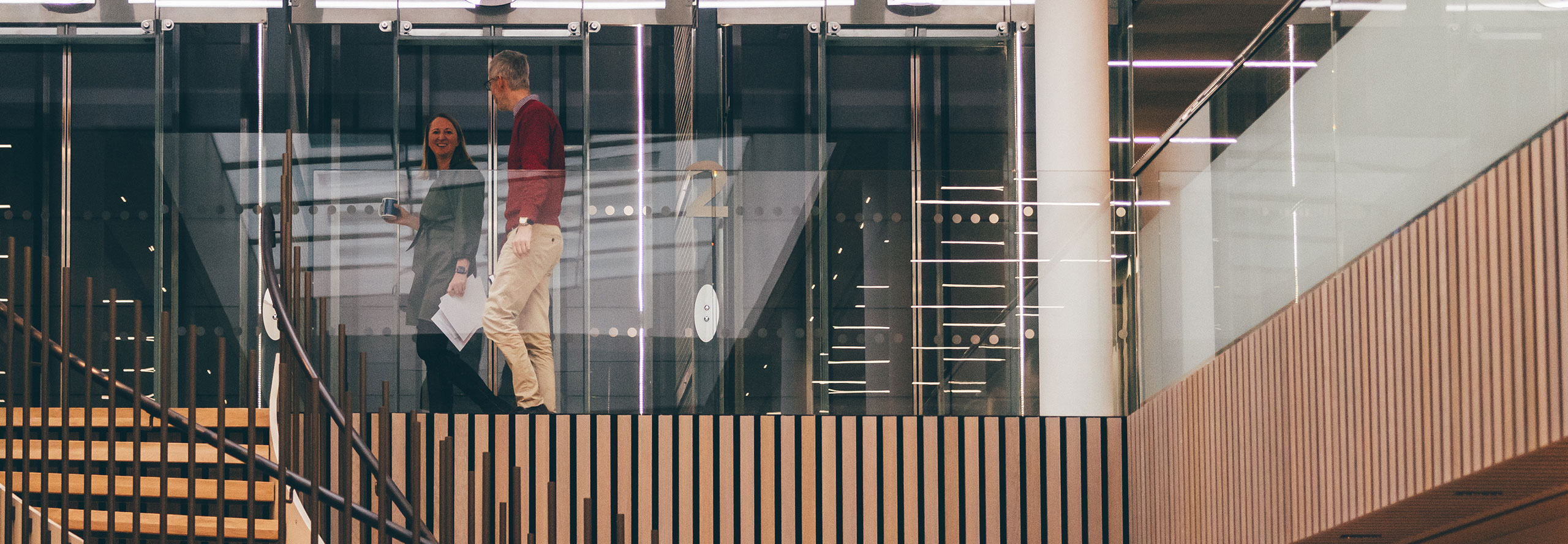 Two people walking along a glass walkway in an office